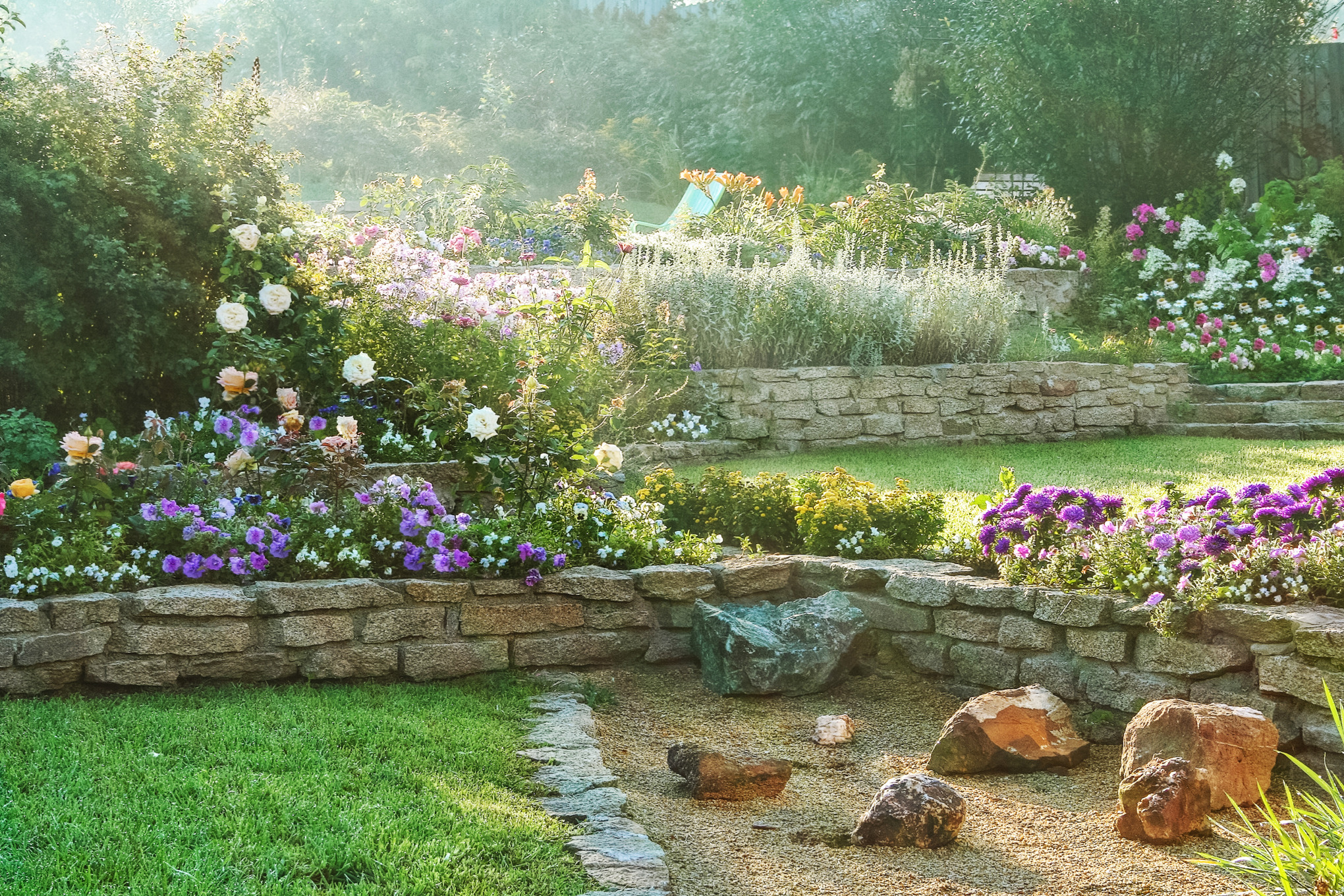 Jardin en pente avec murs en pierre, fleurs multicolores et pelouse