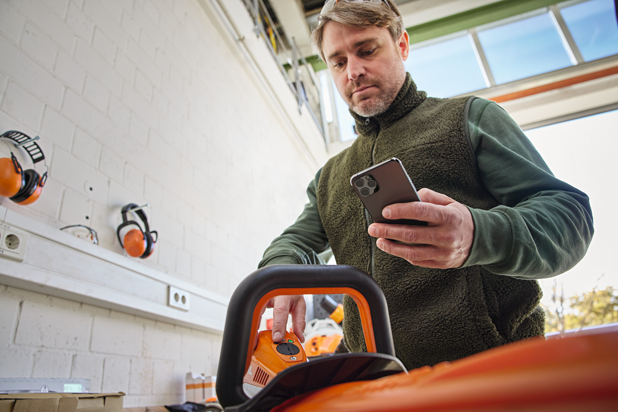 Une personne vérifie l’état de l’appareil sur le Smart Connector 2 A et regarde son smartphone avec l’application STIHL connected