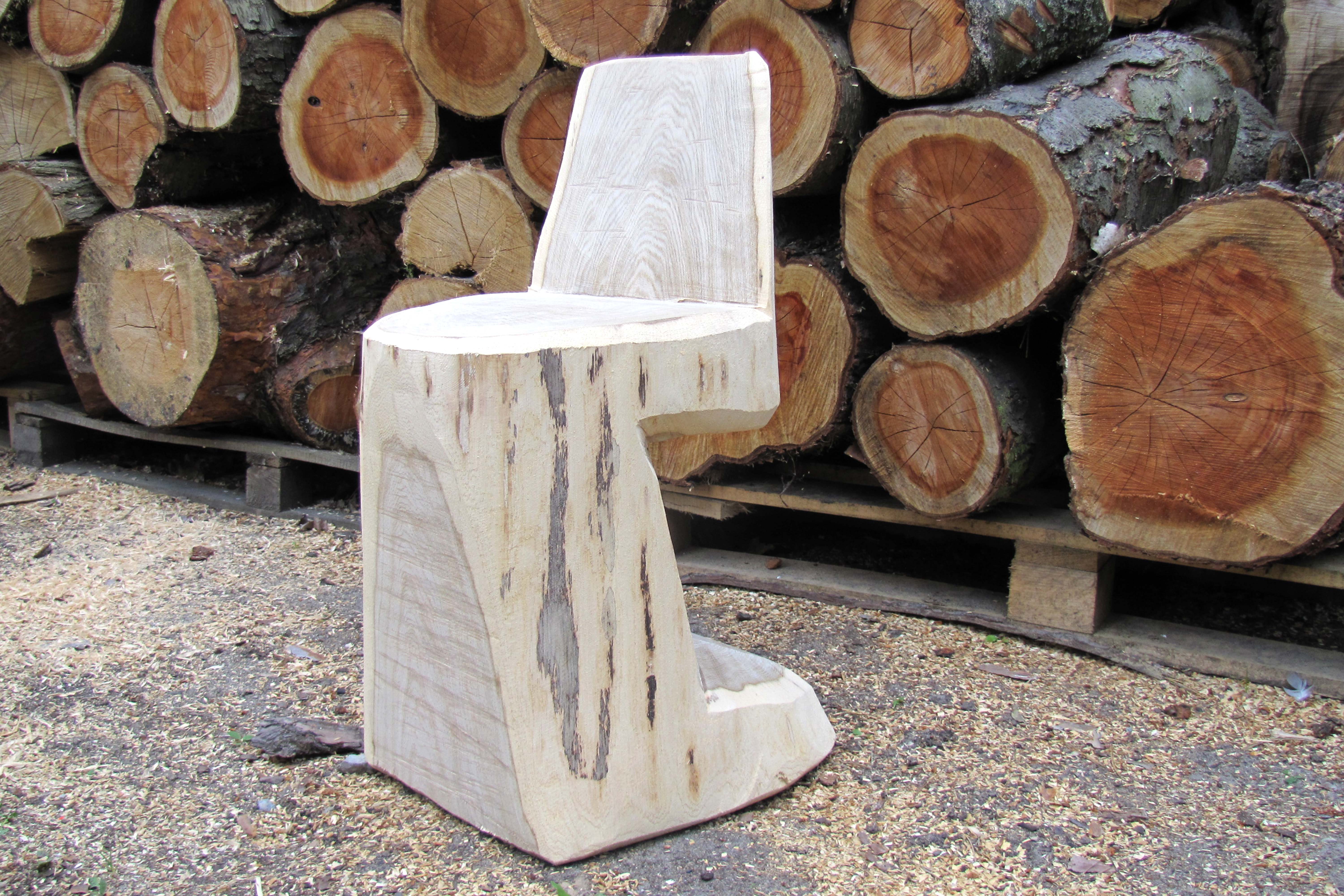 Une chaise en rondin de bois terminée devant un tas de troncs d’arbres