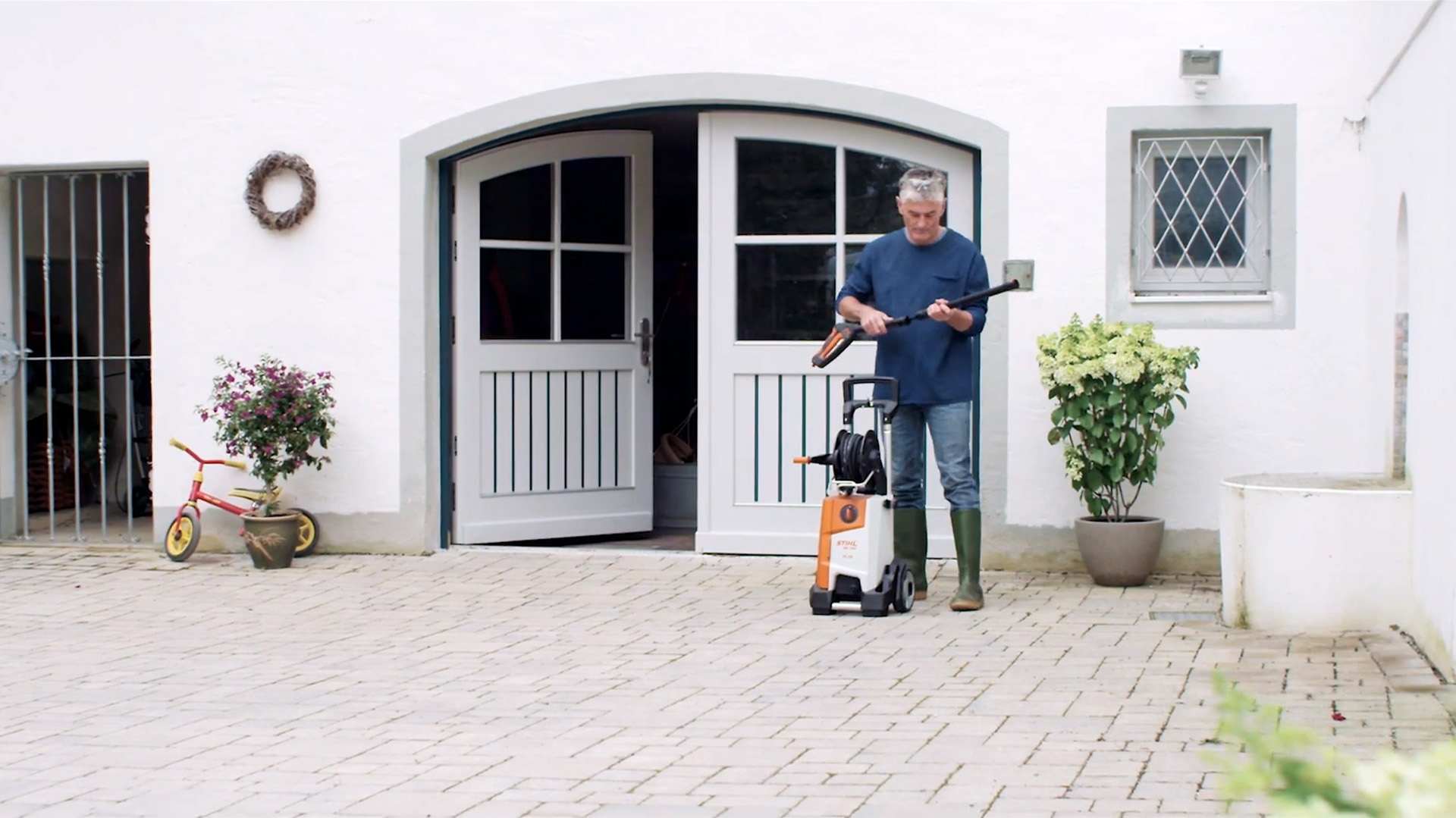 Homme debout devant une maison blanche, se préparant à nettoyer l’extérieur avec un nettoyeur haute pression STIHL