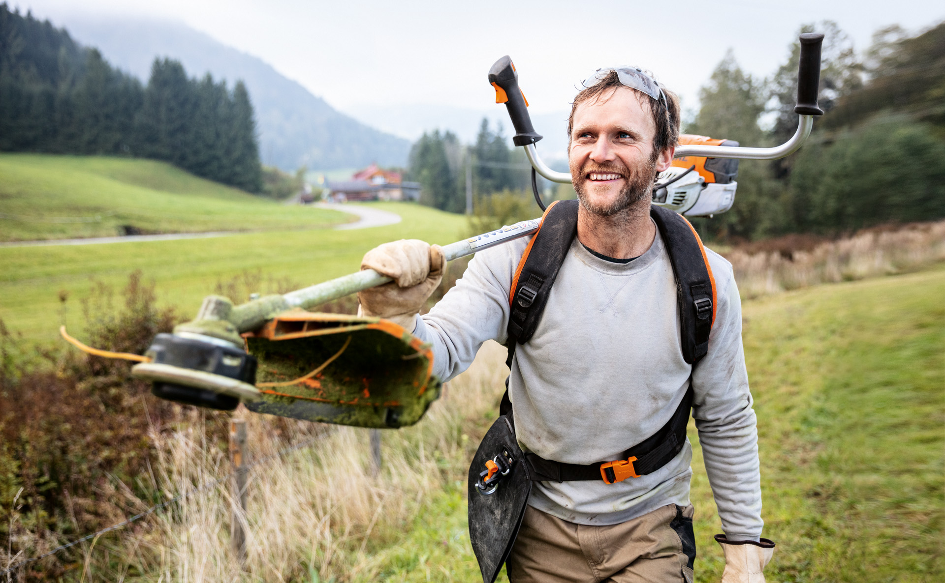 Un homme souriant avec une débroussailleuse STIHL FS 91 sur l’épaule en train de traverser un champ