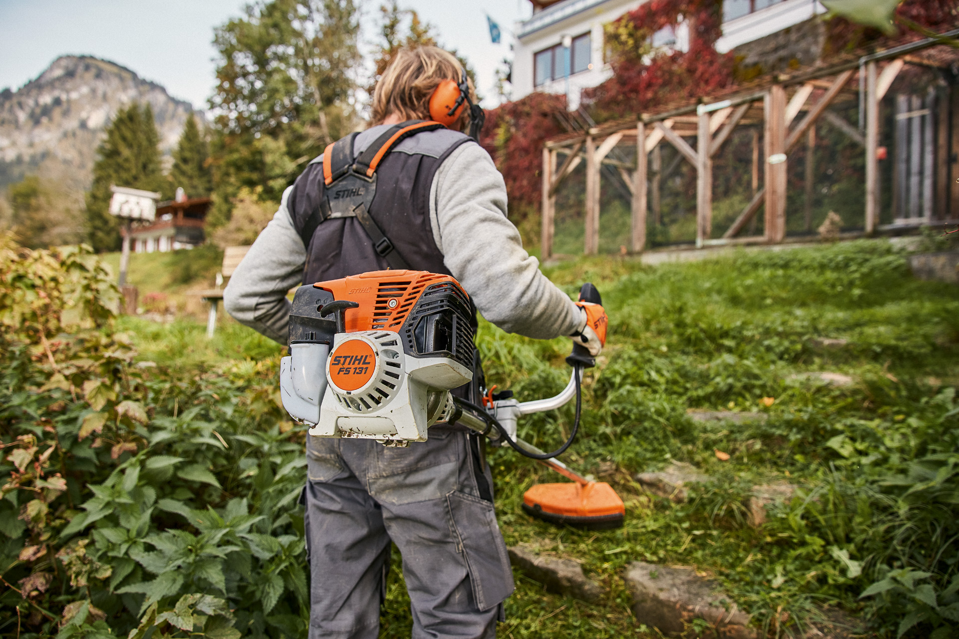 Une personne munie d’un équipement de protection utilise la débroussailleuse thermique STIHL FS 131 dans un jardin en pente