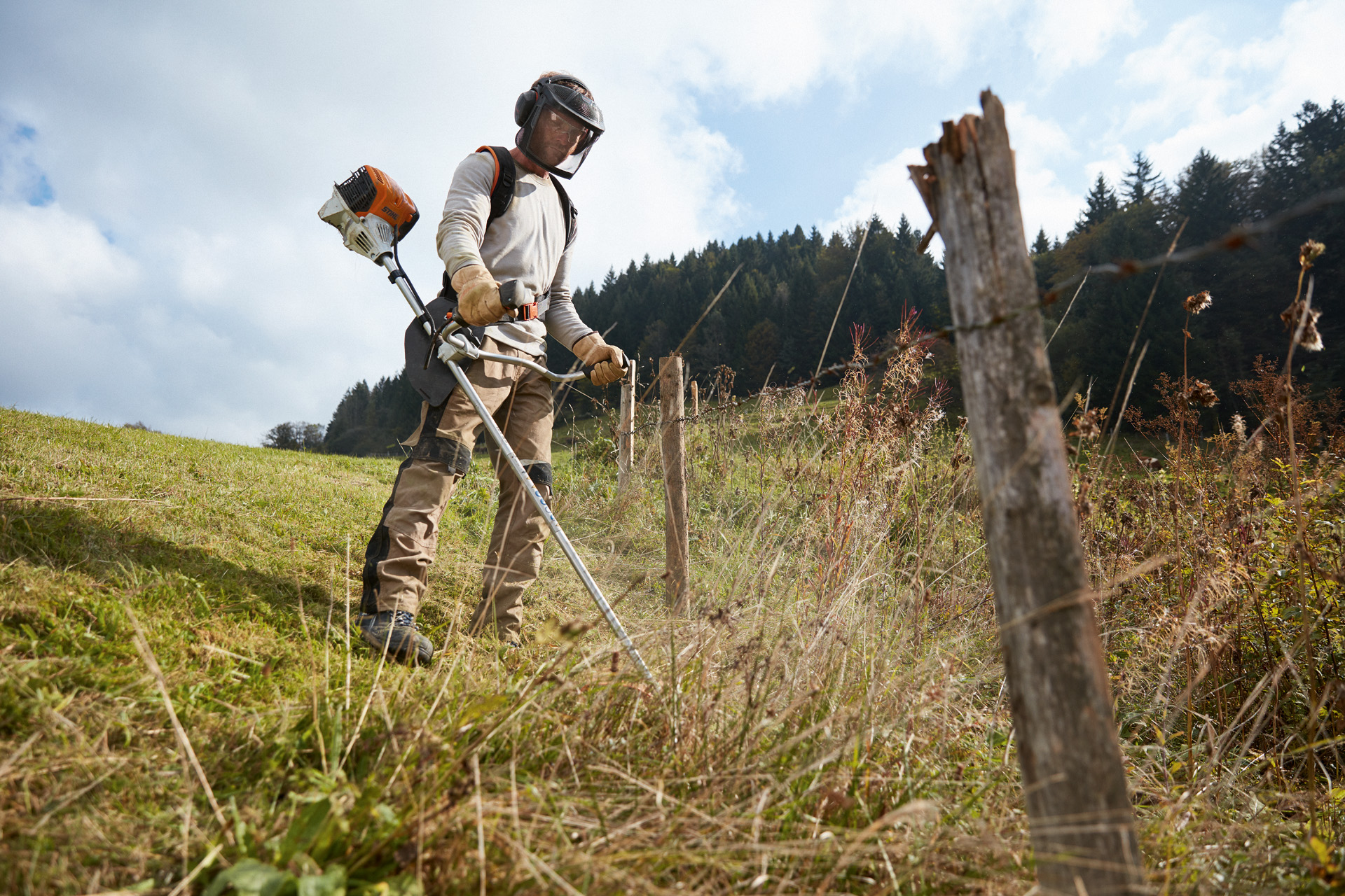 Un homme en équipement de protection tond le gazon avec un coupe-bordures à essence STIHL FS 91