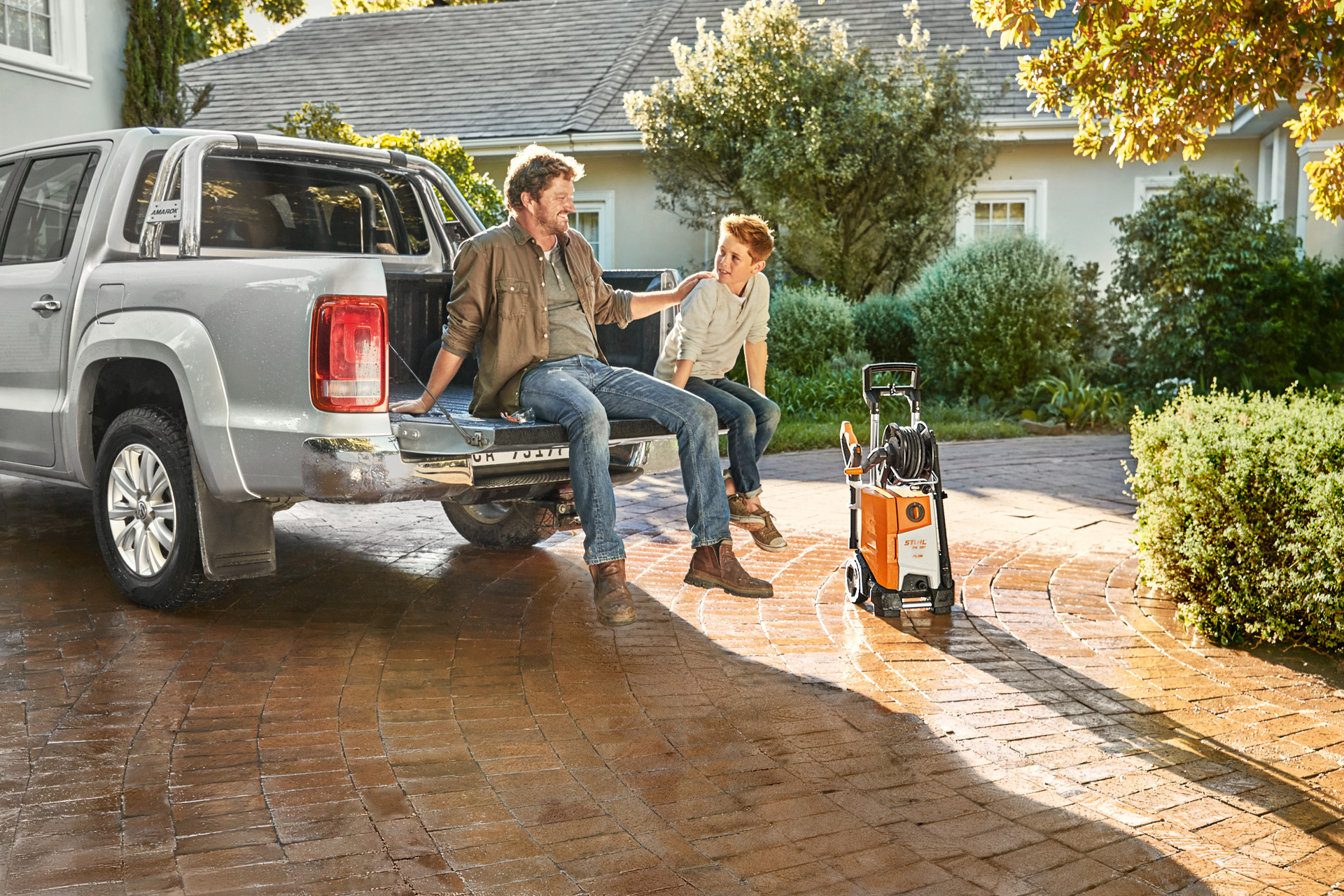 Homme & enfant assis sur le plancher d’une camionnette, le nettoyeur haute pression STIHL RE 130 Plus à côté du véhicule