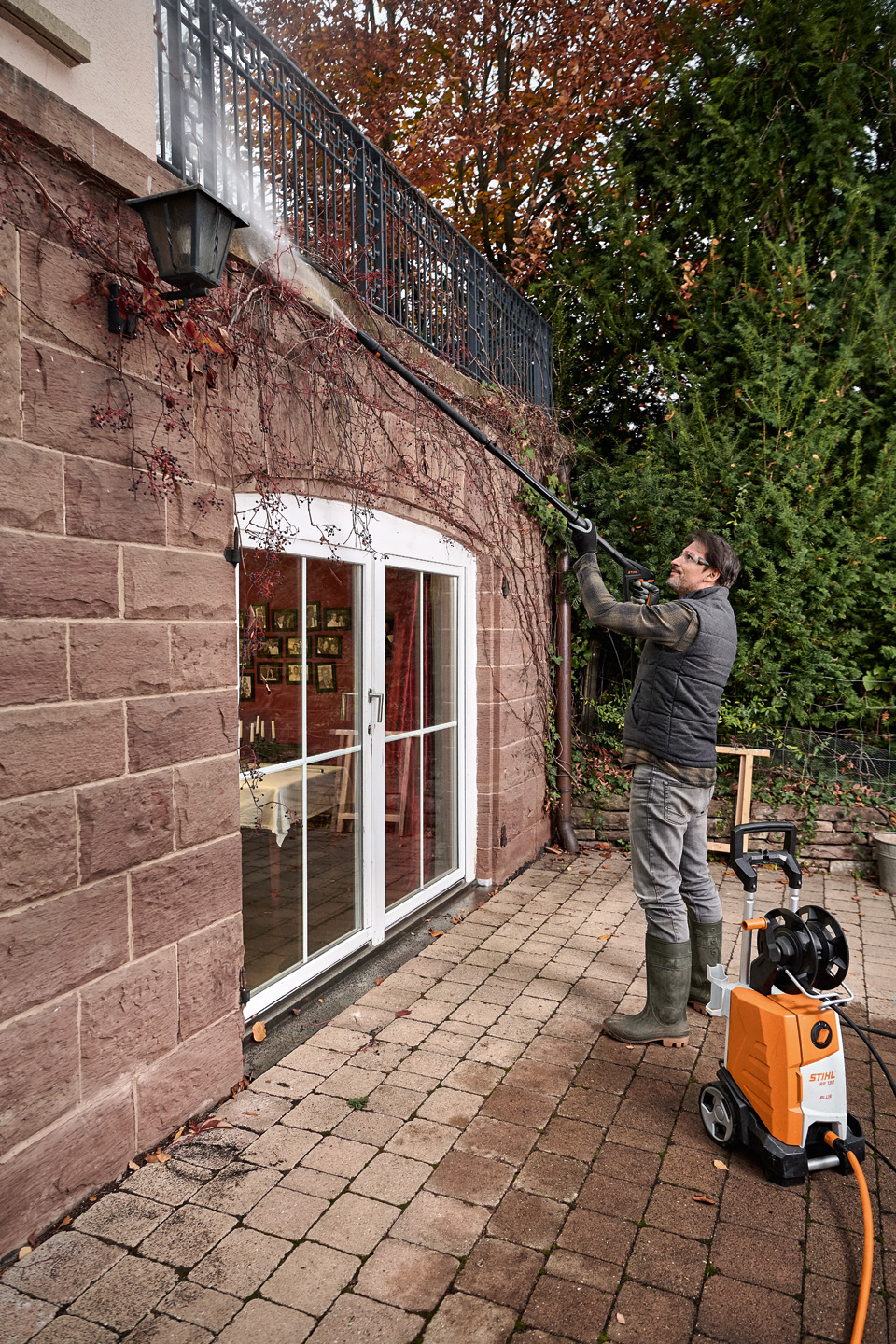 Homme debout sur une terrasse et nettoyant l’extérieur d’une maison à l’aide d’un nettoyeur haute pression STIHL
