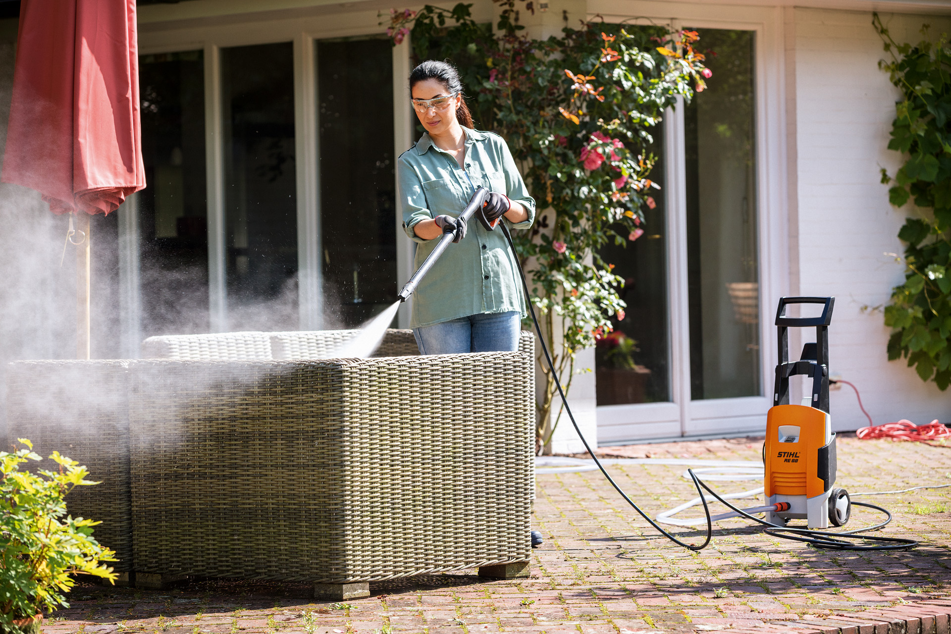Une femme portant des lunettes de protection nettoie ses meubles de jardin sur la terrasse avec le nettoyeur haute pression STIHL RE 88.
