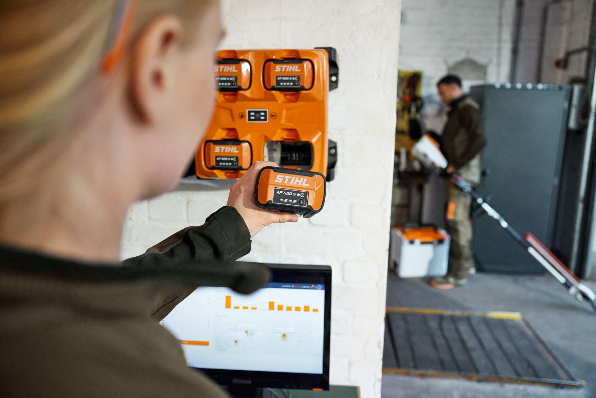 Une femme devant un ordinateur portable retire un AP 300 S du chargeur multiple STIHL AL 301-4