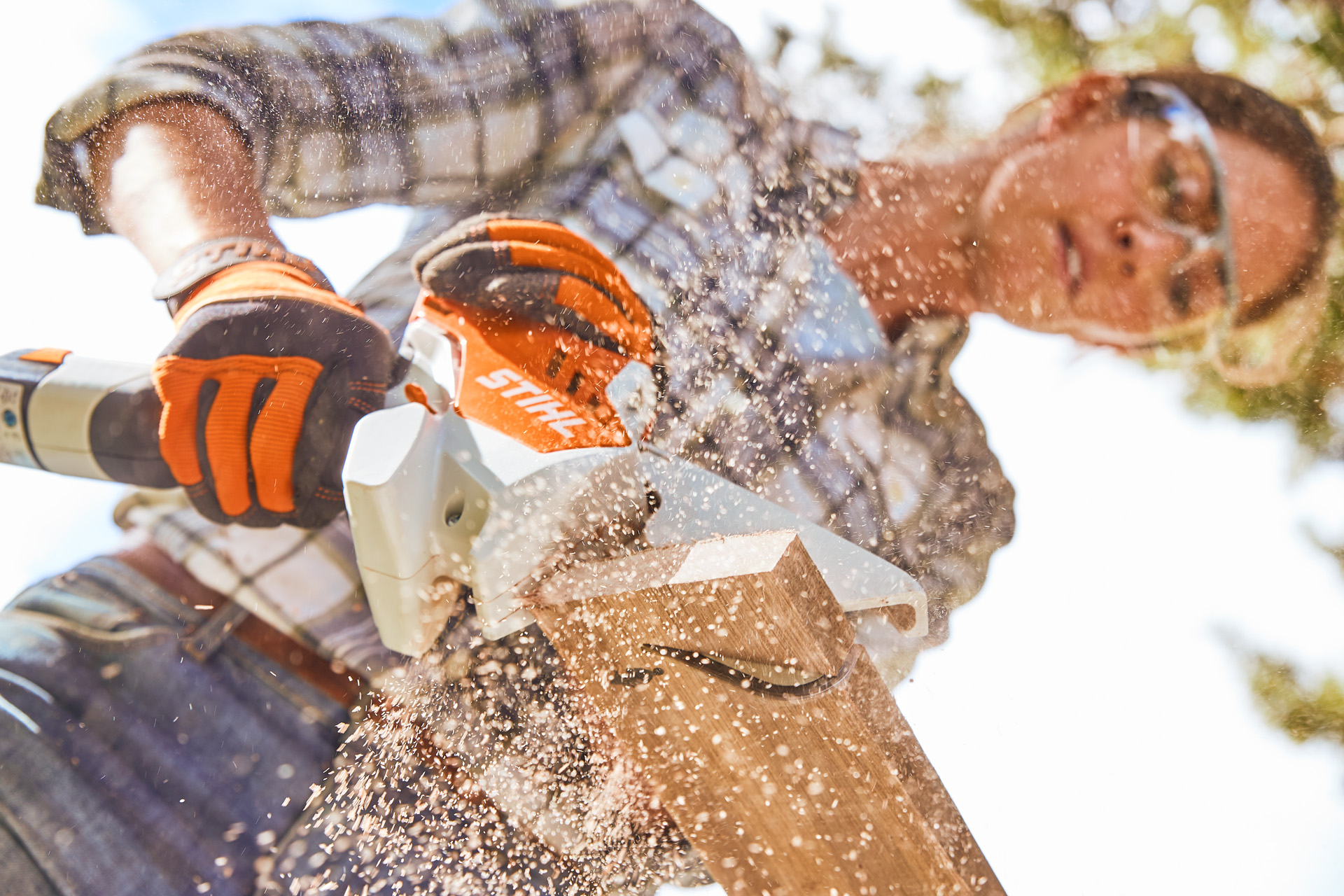 Une femme, munie de lunettes de protection, coupe un morceau de bois avec une scie de jardin sur batterie STIHL GTA 26