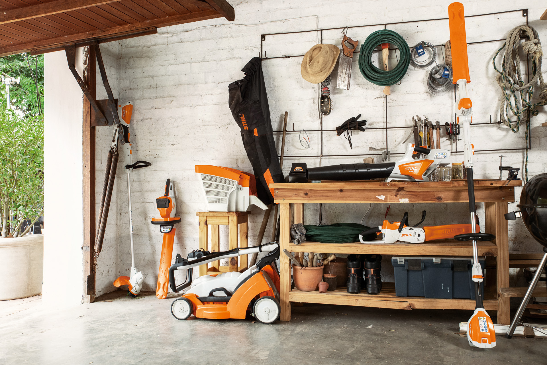 Intérieur d’un garage avec un coupe-bordure STIHL FSA 56 sur batterie et un taille-haie STIHL HSA 56 sur batterie posés contre le mur, et une tondeuse RMA 339 sur batterie juste à côté