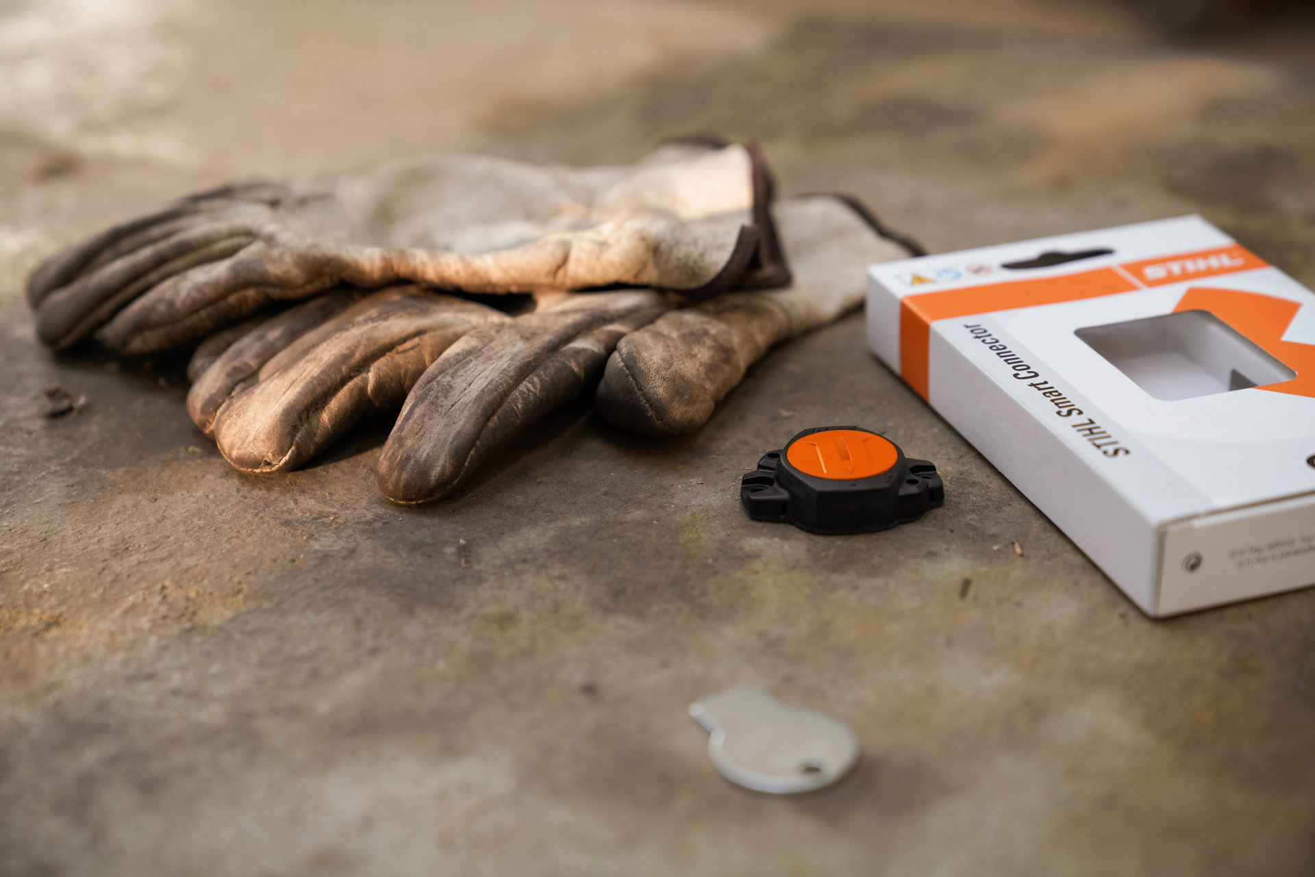 Le smart connector STIHL pose à côté de son packaging et d’une paire de gants de protection