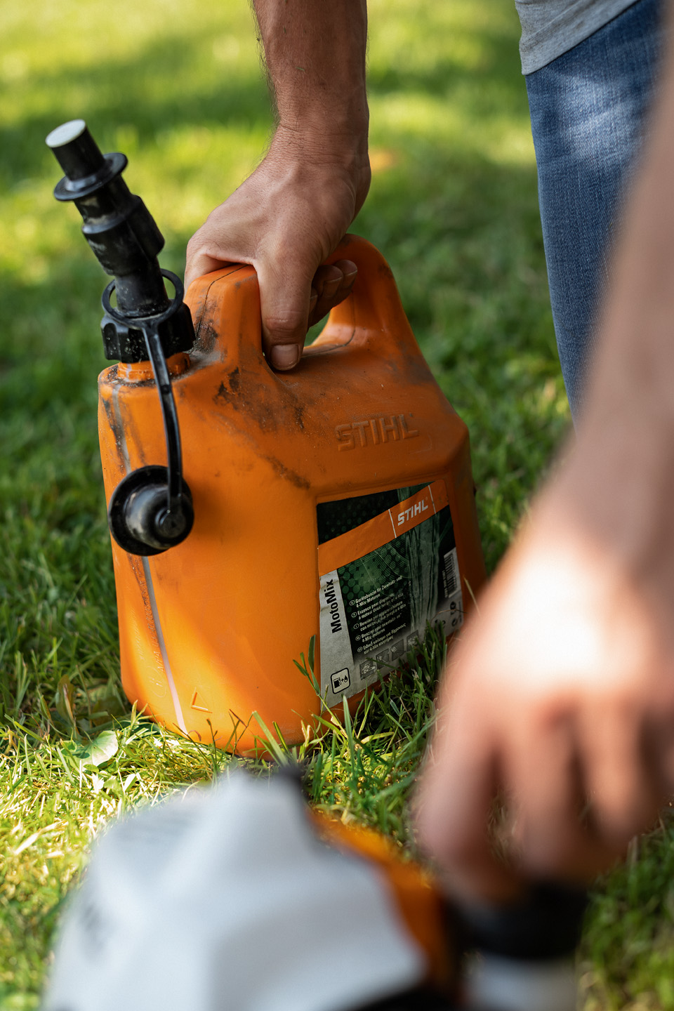 Bidon de carburant STIHL MotoMix ouvert posé sur le sol, avec une main dévissant le bouchon du réservoir d’un coupe-bordure