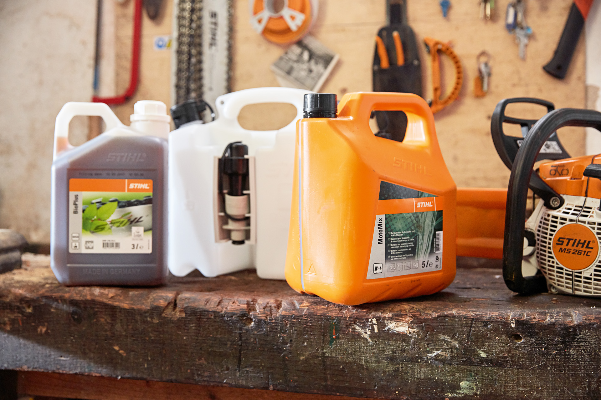 Un bidon de remplissage sur un banc entre des bidons d’huile pour chaîne STIHL MotoMix et BioPlus, avec une tronçonneuse thermique STIHL MS 261 C à l’arrière