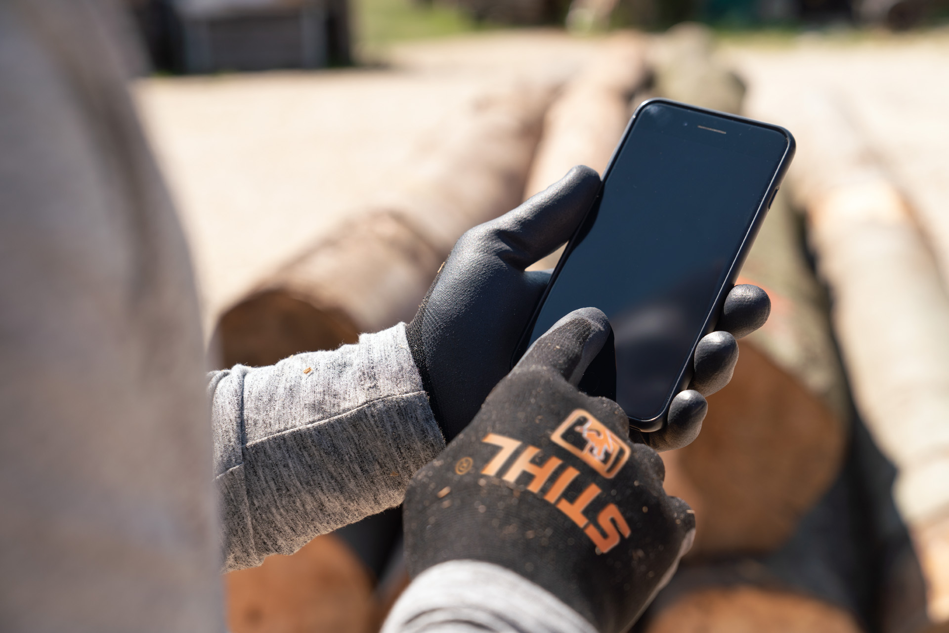 Un homme portant des gants de protection STIHL et touchant son écran de smartphone