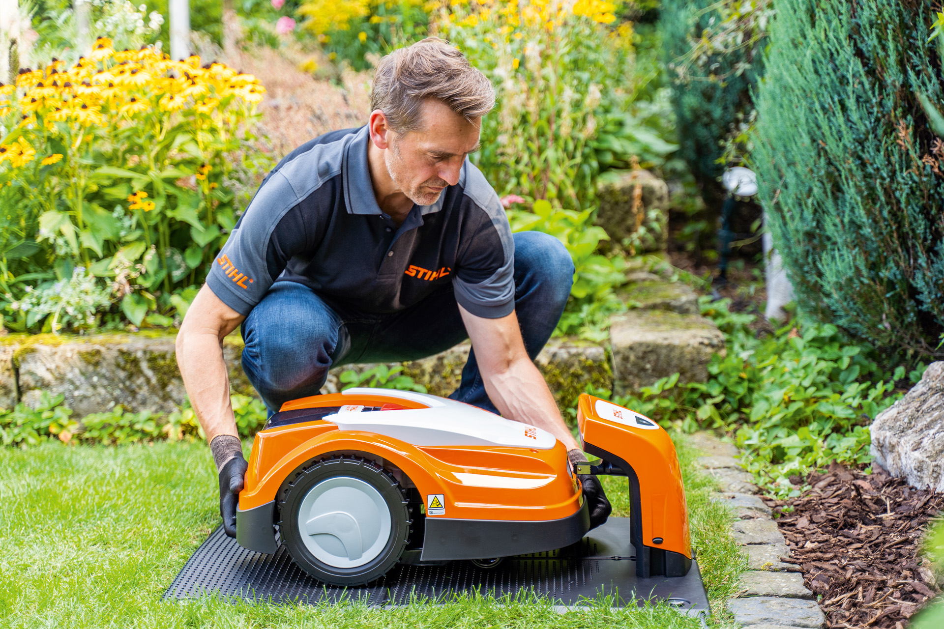 Un revendeur STIHL place un robot de tonte STIHL iMOW dans sa station de charge dans un jardin.