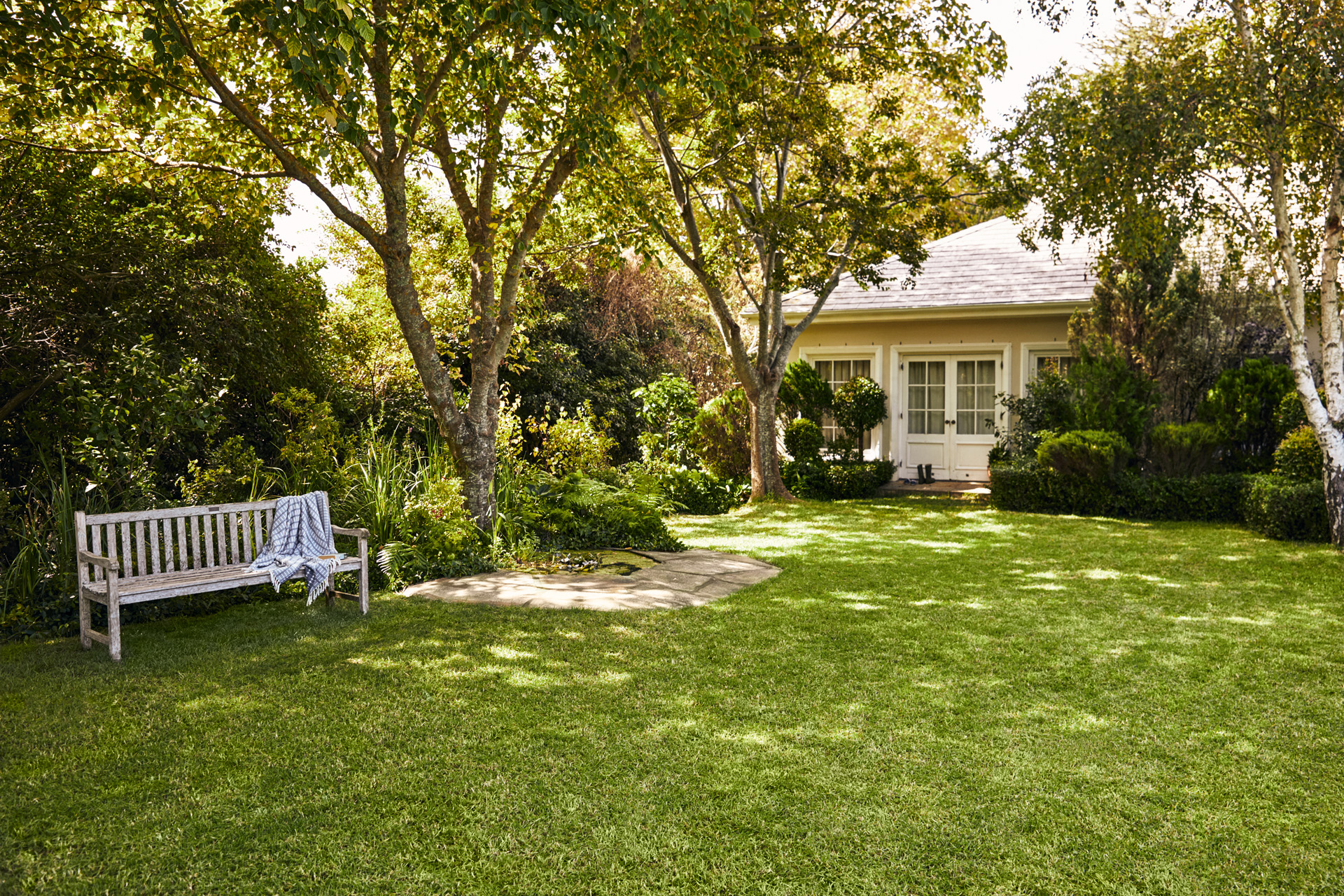 Petite maison avec jardin, au premier plan un banc de jardin sur une pelouse verte