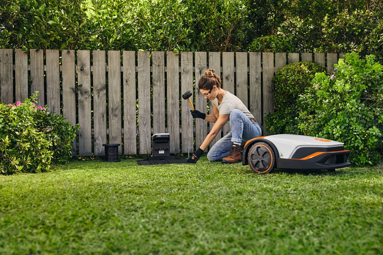 Femme dans un jardin, un marteau à la main, installant la station d’accueil iMOW®