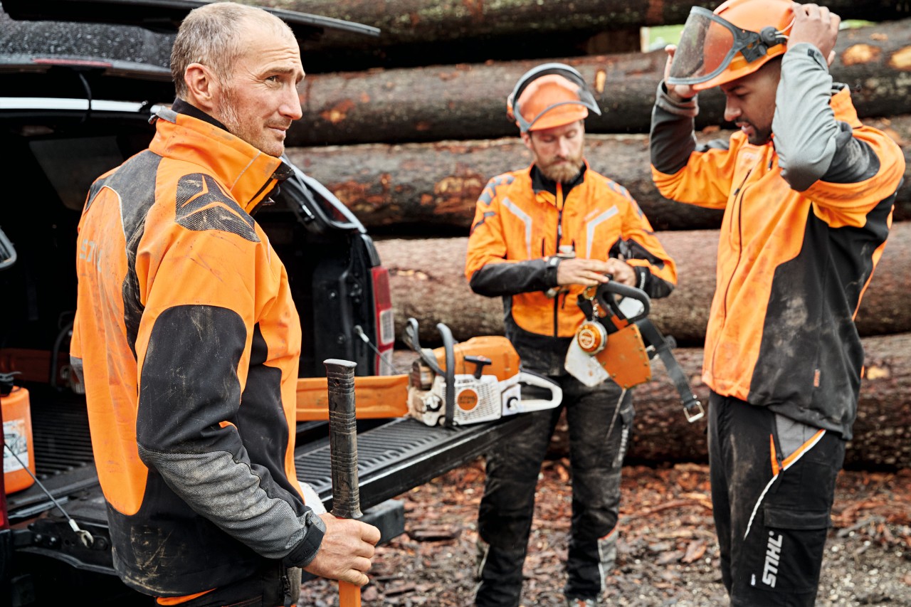 Trois hommes en équipement de protection devant un véhicule avec le coffre ouvert, contenant des appareils à batterie STIHL