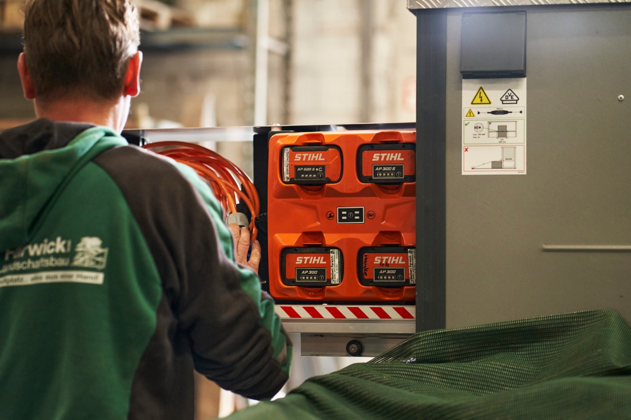 Un employé de Farwick GmbH vu de dos se trouve devant un bottTainer powered by STIHL