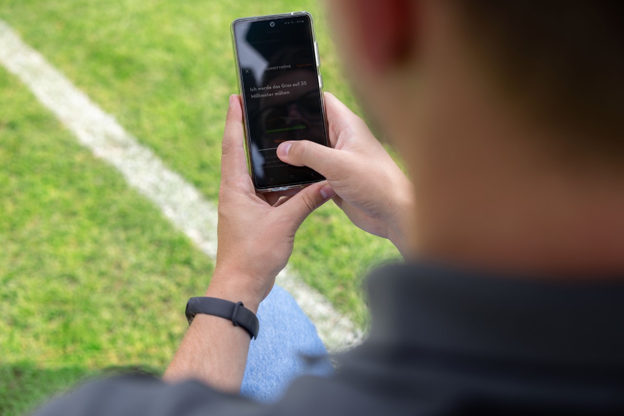 Une personne sur un terrain de sport a ouvert l’application MY iMOW® sur un téléphone portable
