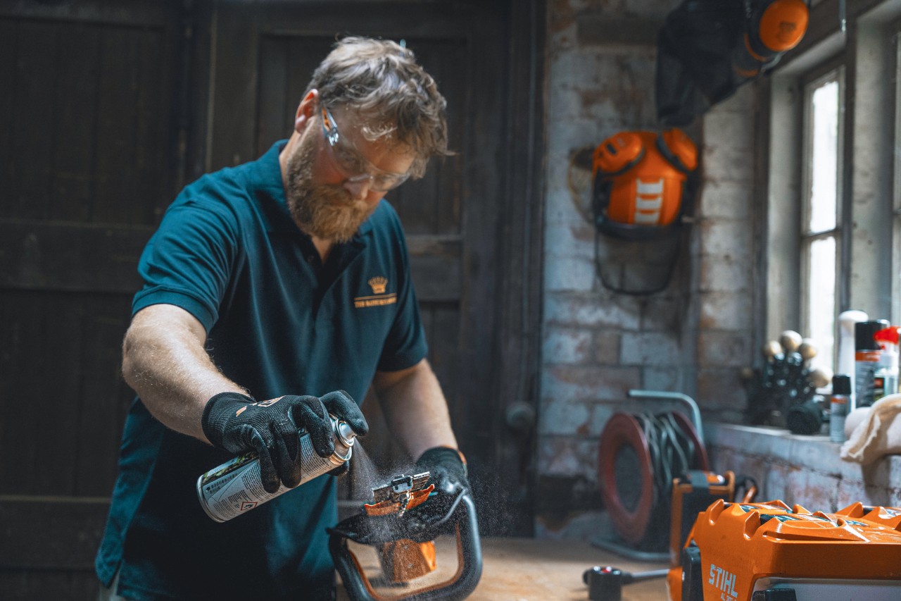 Un homme dans un atelier pulvérise STIHL Superclean sur un taille-haies