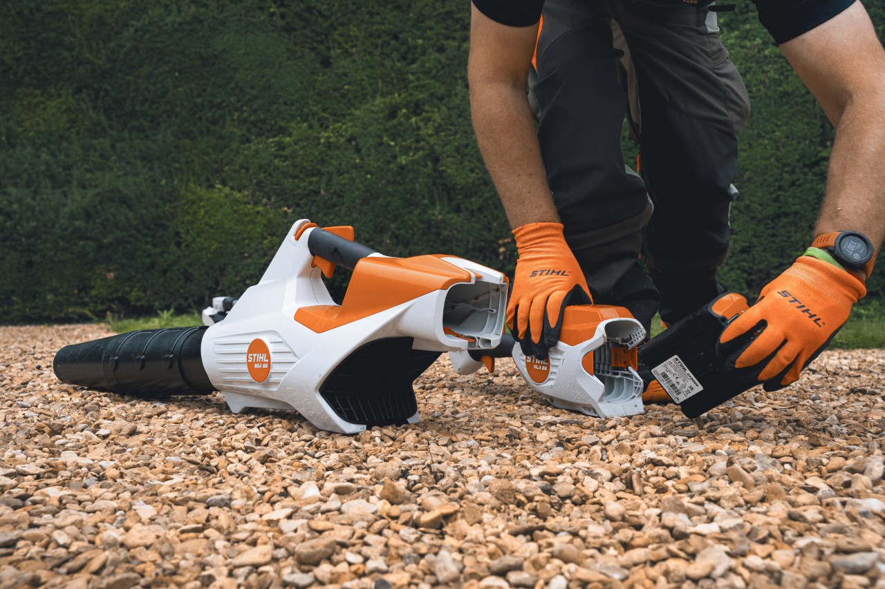 Un professionnel remplace la batterie de son souffleur à batterie STIHL devant la haie du Bathurst Estate