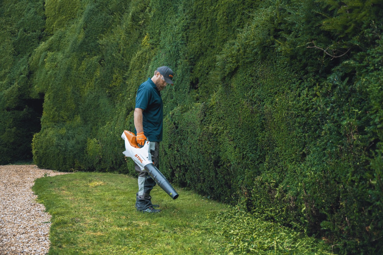 Un professionnel avec un souffleur à batterie STIHL devant la haute haie de Bathurst Estate