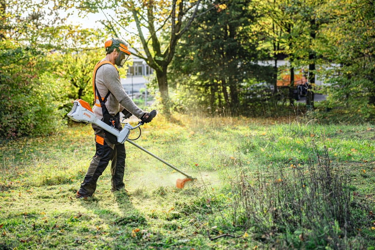 Un homme tond un espace vert dans un parc avec la débroussailleuse à batterie STIHL FSA 200