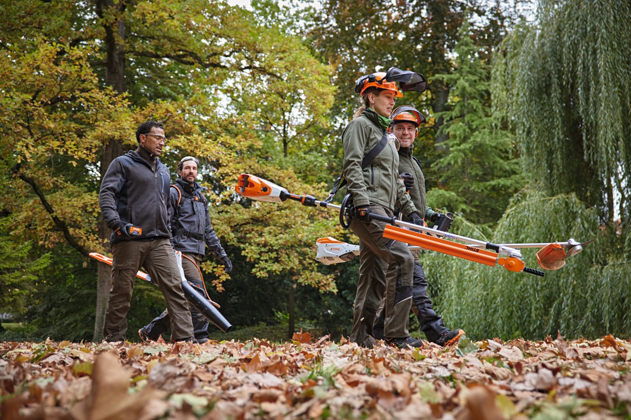 Quatre professionnels STIHL avec des appareils à batterie marchent le long d’un chemin