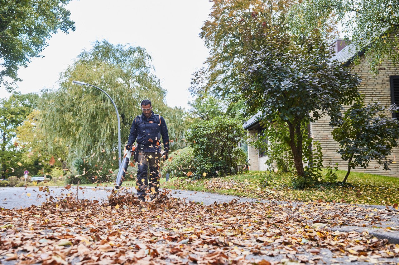Un jardinier paysagiste enlève les feuilles mortes d’une route avec le souffleur de feuilles sur batterie STIHL BGA 200.