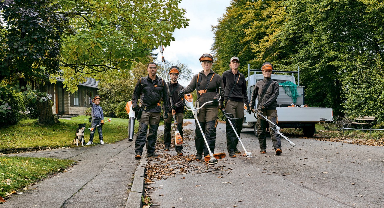 Équipe de jardiniers et de paysagistes avec des machines à batterie professionnelles de STIHL marchant dans une rue.