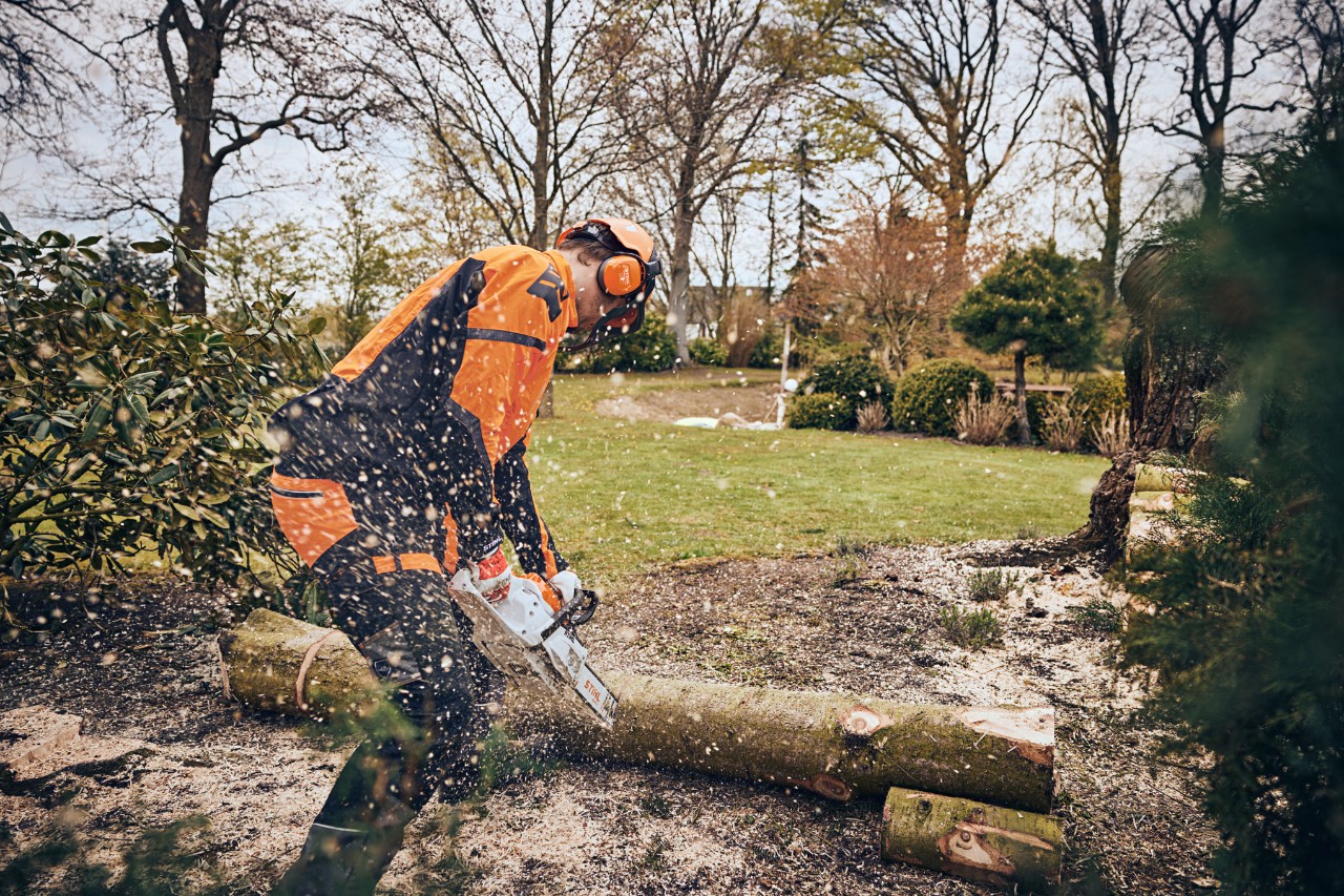 Homme en équipement de protection découpant un tronc d’arbre dans un espace vert avec une tronçonneuse à batterie STIHL