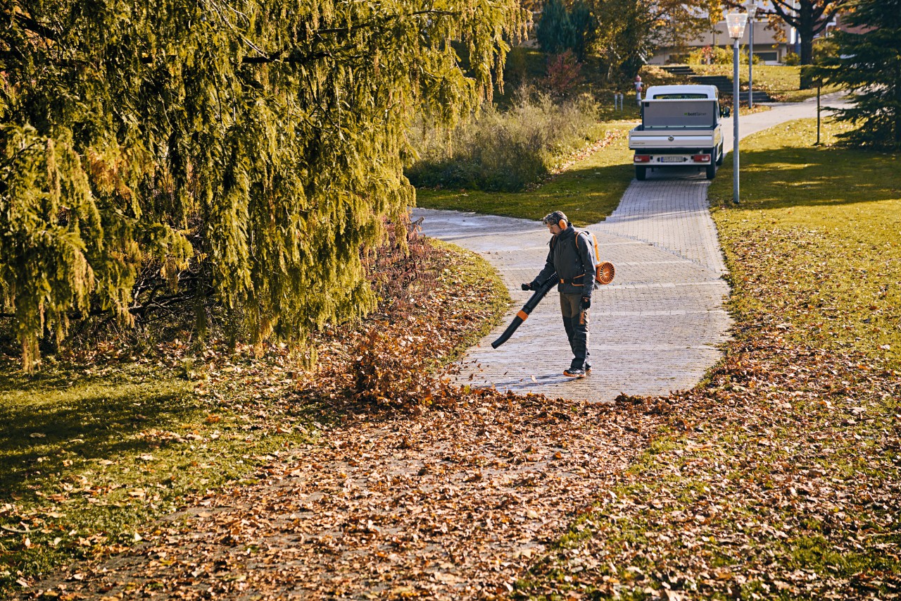 Un homme en équipement de travail enlève les feuilles d’un chemin à l’aide d’un souffleur de feuilles à batterie
