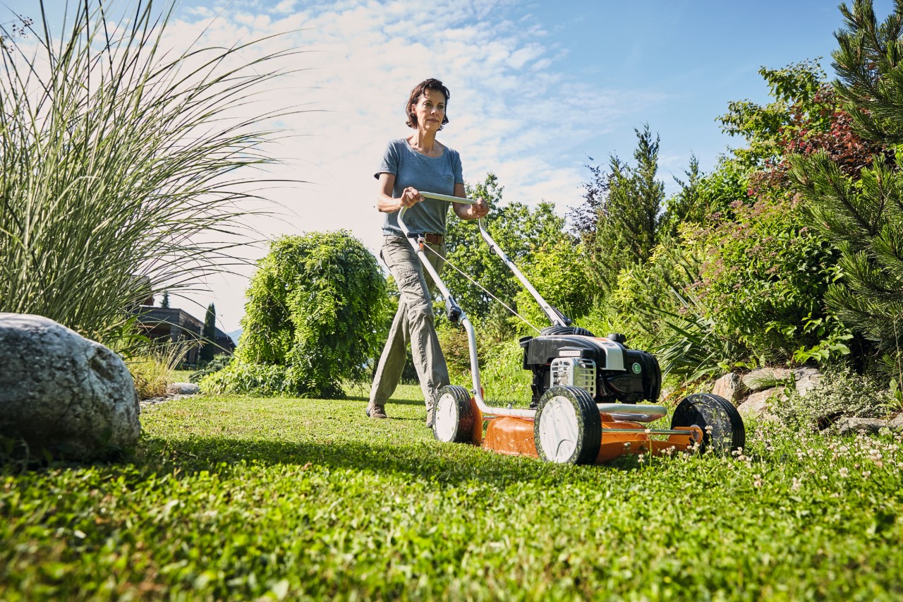 Une femme déchiquette sa pelouse à l'aide d'une tondeuse mulching à essence