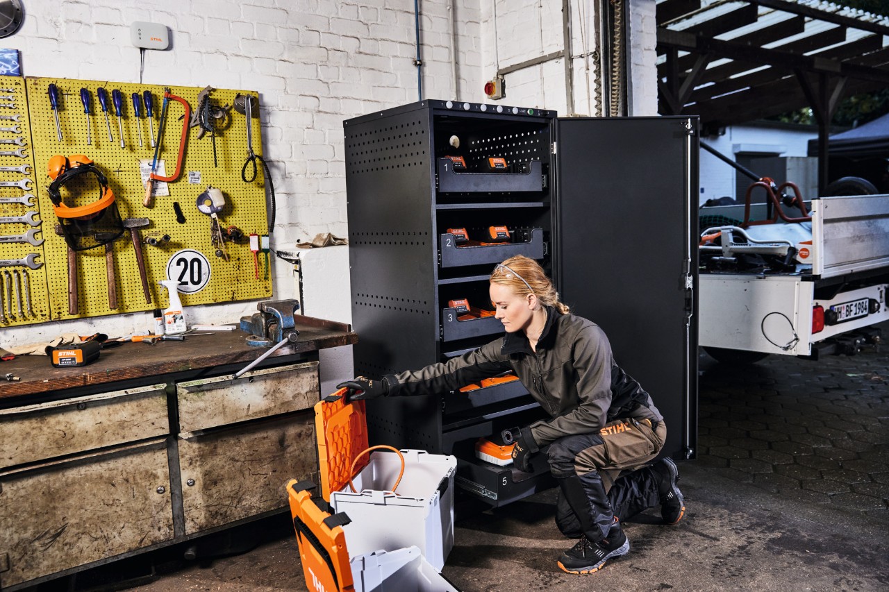 Femme en tenue de travail STIHL dans un atelier avec armoire de charge de batteries et STIHL connected Box
