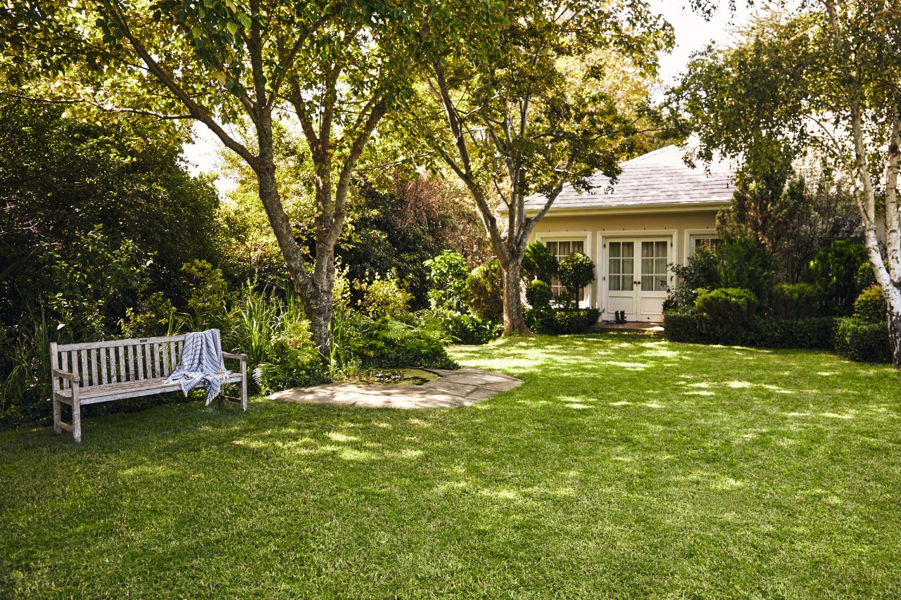 Petite maison avec jardin, au premier plan un banc de jardin sur une pelouse verte