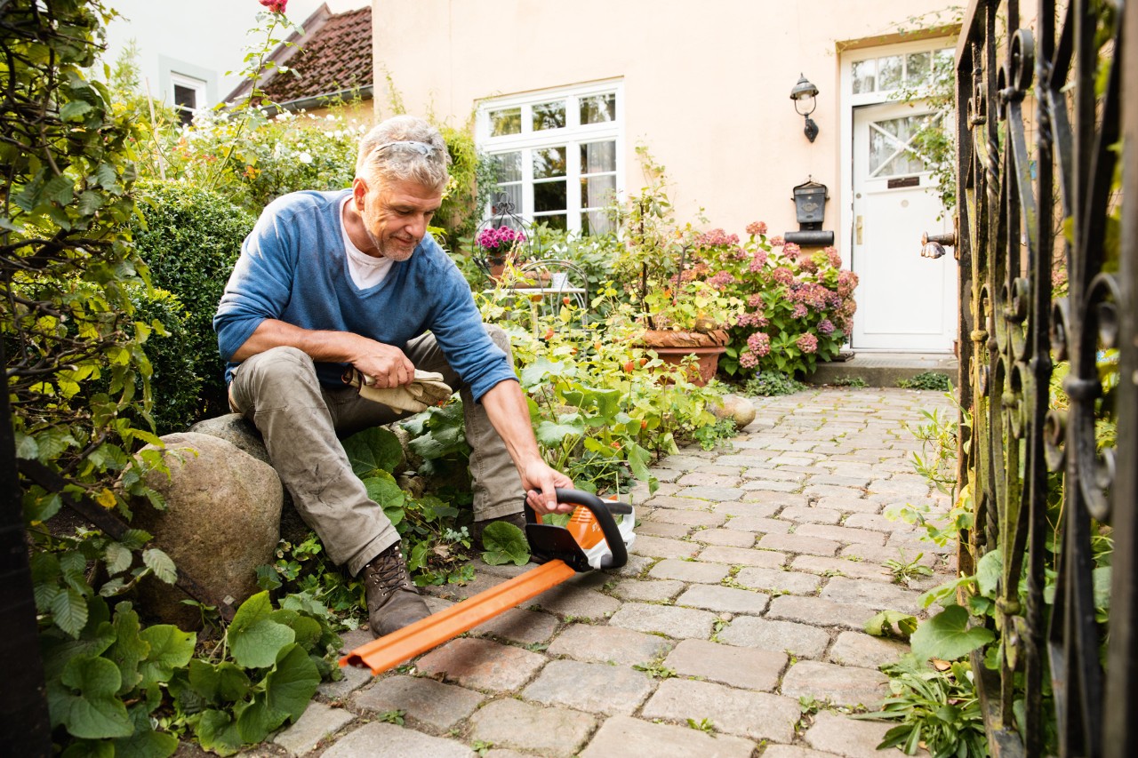 Un homme maniant un taille-haies à batterie HSA 45 de la série AI d’outils STIHL devant une maison